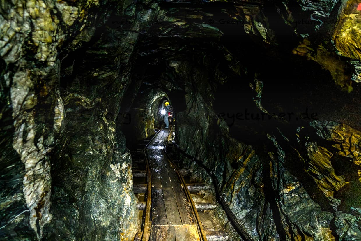 Ein Besucher mit Stirnlampe beleuchtet einen dunklen Bergbaustollen am Wasserfallrundweg Untersulzbach Rosental Austria