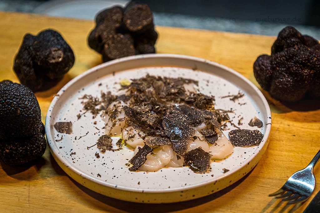 Frische Jakobsmuscheln gewürzt mit Meersalz, schwarzem Pfeffer und Olivenöl sowie frisch gehobeltem schwarzen Trüffel.  Reduziert auf diese wenigen Zutaten kommt das Aroma des schwarzen Trüffels sehr gut zur Geltung / © Foto: Georg Berg