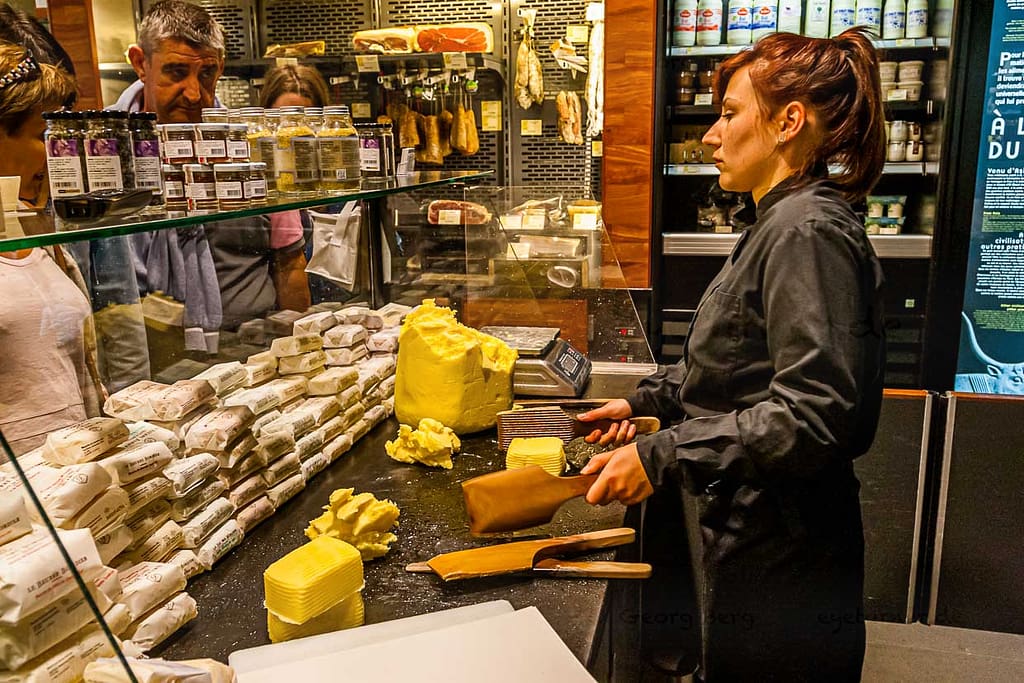 Verkaufstheke im Maison du Beurre von Jean Yves Bordier in Saint Malo. Eine Verkäuferin schlägt die Butter mit zwei Holzpaddeln / © Foto: Georg Berg