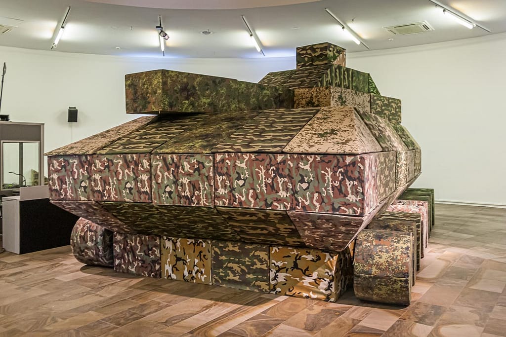 Krieg – immer wieder ein Thema auf der documenta. Sitzmodule in Fleckentarnung werden zweimal in der Woche in einer Performance zu einem Panzer in Originalgröße zusammengebaut / © Foto: Georg Berg