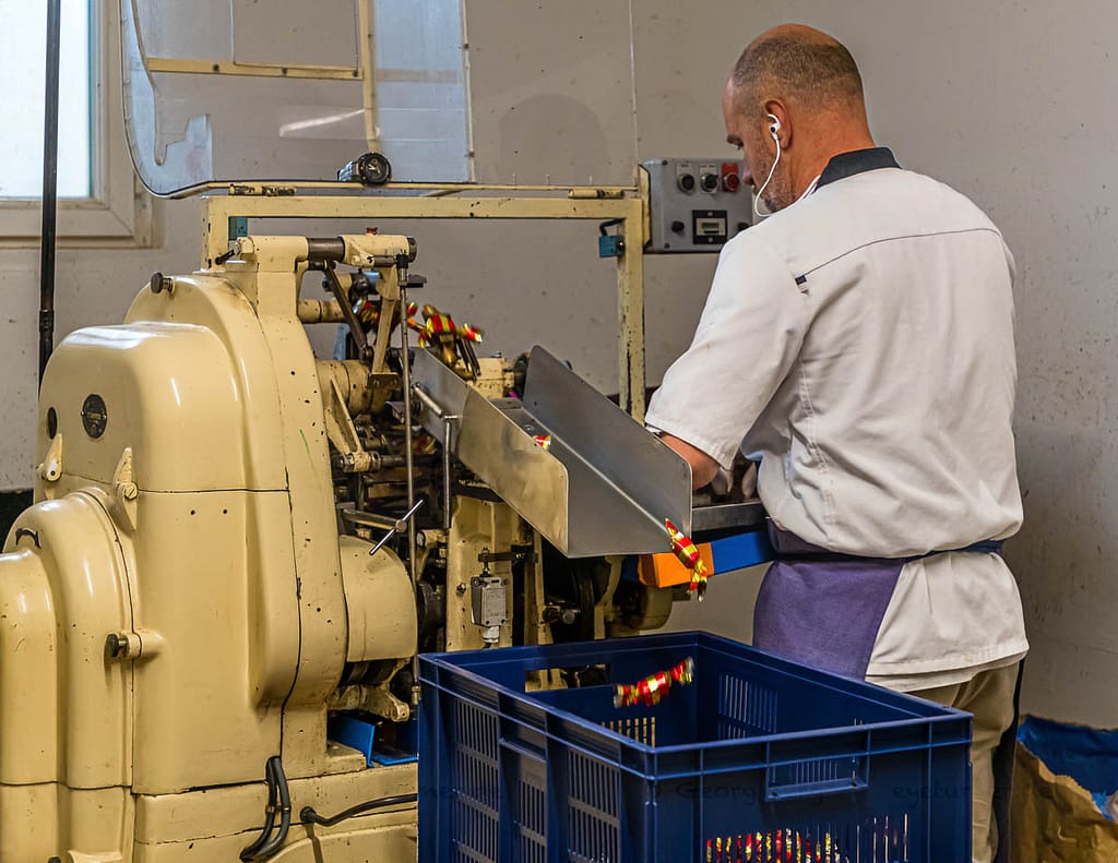 Maschinelle Verpackung von Nuss-Nougat-Pralinen in gold und rot gesteiften Papilloten in der Chocolaterie Frigoulette in Beaufort-sur-Gervanne im Val de Drôme / © Foto: Georg Berg