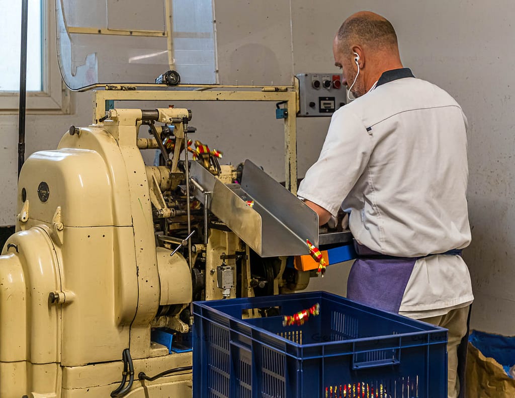 Maschinelle Verpackung von Nuss-Nougat-Pralinen in gold und rot gesteiften Papilloten in der Chocolaterie Frigoulette in Beaufort-sur-Gervanne im Val de Drôme / © Foto: Georg Berg