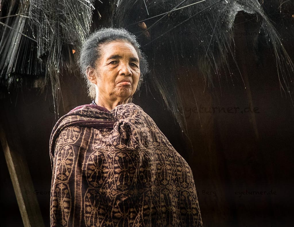 Frau in traditioneller Kleidung vor einer Hütte in Wologai, Indonesien / © Foto: Georg Berg