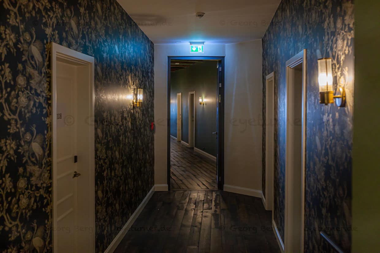 Die Gänge zu den Zimmern sind schief und charmant. Die Wände tragen wahlweise ausgefallene Tapeten, Lehmputz mit umweltfreundlichen Wandfarben auf Basis von Kartoffelstärke oder altes Klostergestein / © Foto: Georg Berg