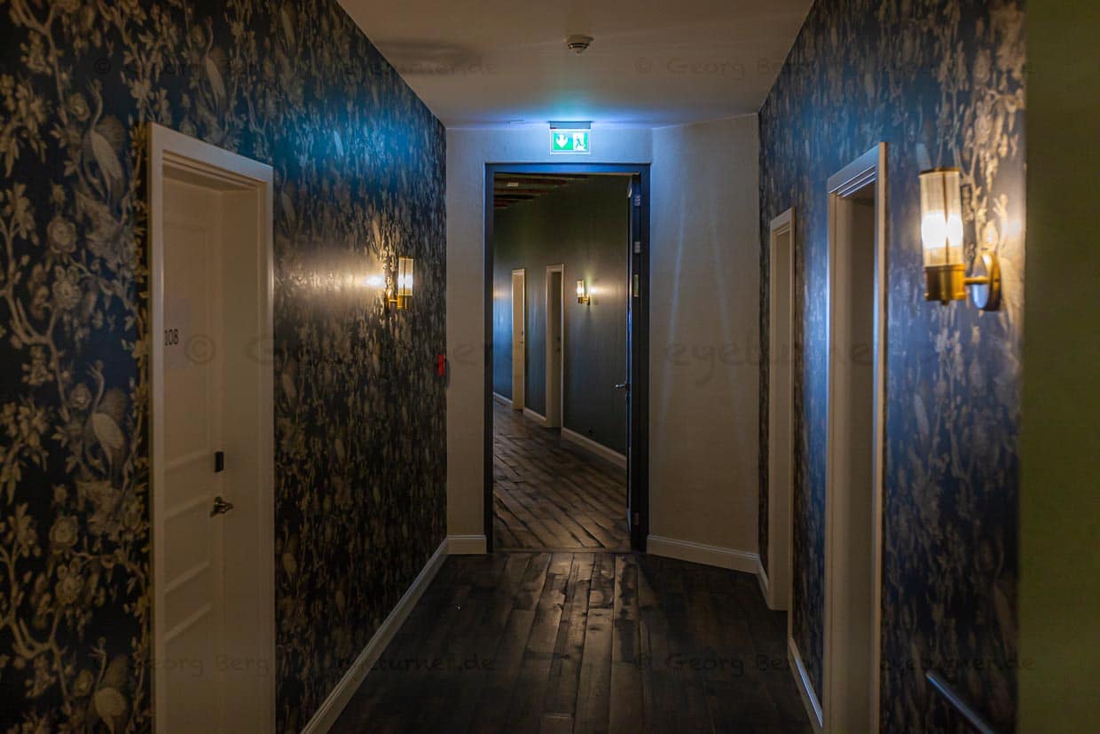 Die Gänge zu den Zimmern sind schief und charmant. Die Wände tragen wahlweise ausgefallene Tapeten, Lehmputz mit umweltfreundlichen Wandfarben auf Basis von Kartoffelstärke oder altes Klostergestein / © Foto: Georg Berg