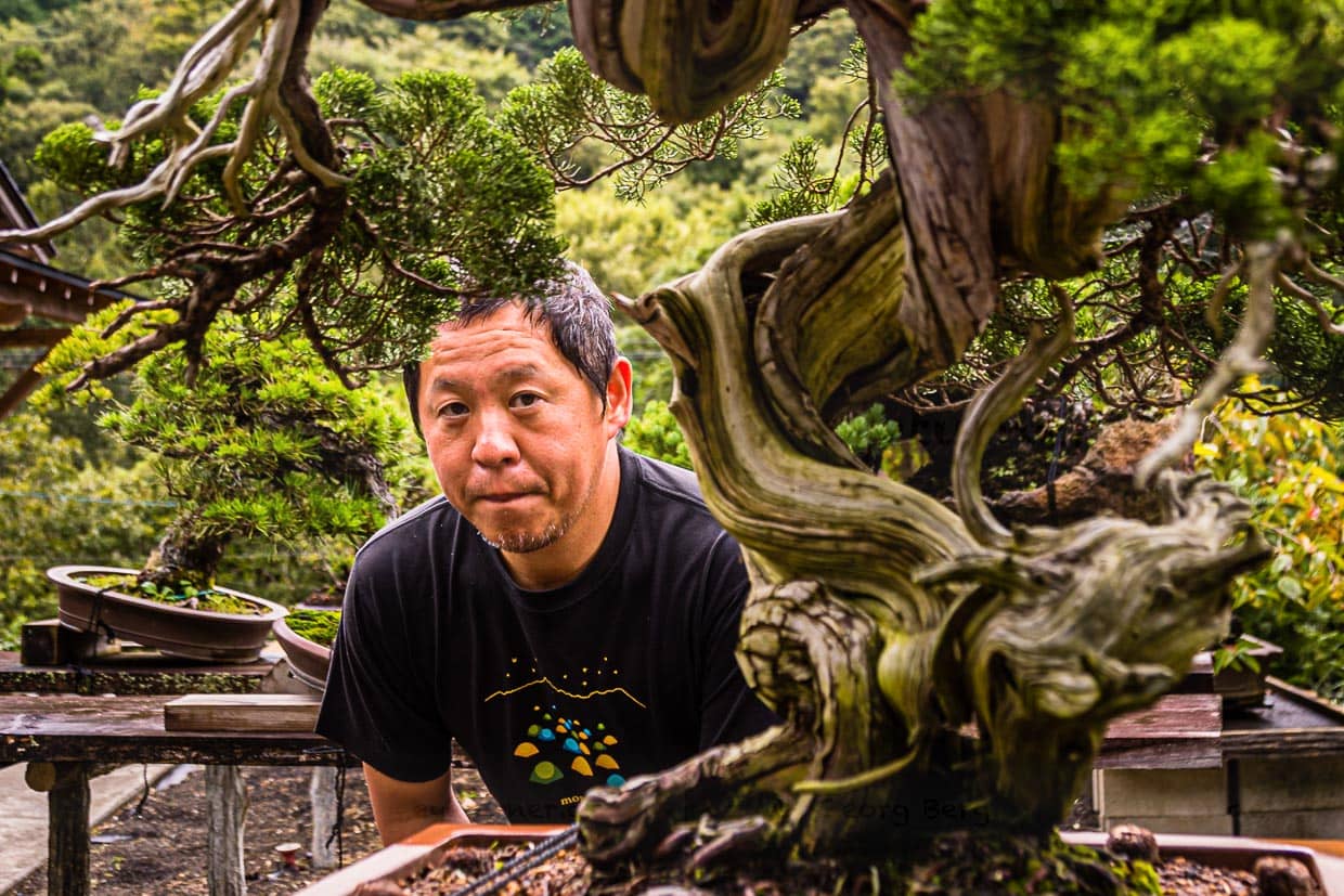 Bonsai-Meister und Garten-Inhaber Toshio Ohsugi im Porträt mit einem 500 Jahre alten Pflegefall. Der Baum wurde den Aufzeichnungen nach um 1920 aus den Bergen von einem Felsen genommen. Seine Wurzeln hatten einen Spalt in den Fels getrieben / © Foto: Georg Berg