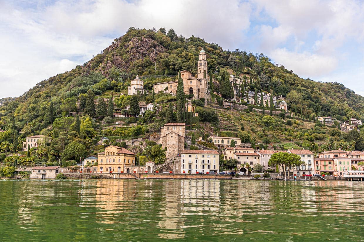 Vom Wasser aus betrachtet: Die Kirche Santa Maria del Sasso von Morcote, darunter die historische Altstadt. Viele kleine Restaurants säumen die Uferpromenade