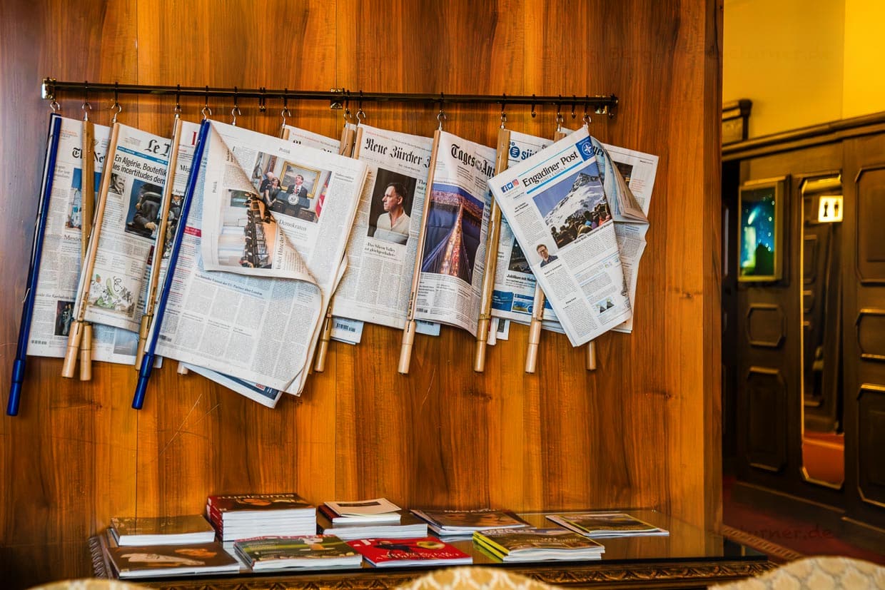 Eine Auswahl an Zeitungen hängt an ihren Spannern in der Bibliothek des Traditionshotels Waldhaus Sils / © Foto: Georg Berg