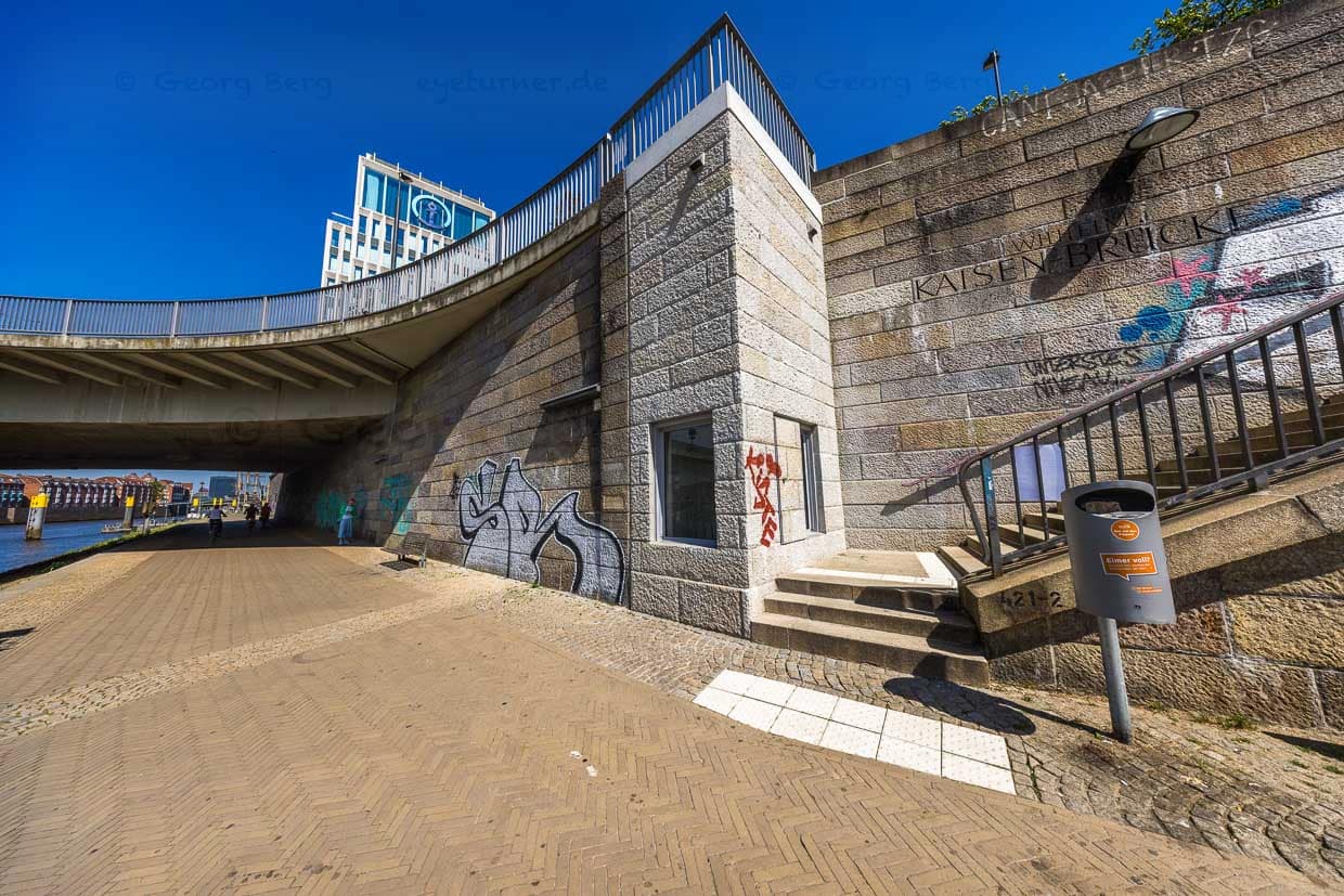 Das Arisierungs-Mahnmal an der Weserpromenade Bremen erinnert seit 2023 an die systematische Enteignung und Ausraubung der Juden während der Zeit des Nationalsozialismus. Entwurf von Evin Oettingshausen. Das Mahnmal steht dort, wo Schiffe damals die geraubten Möbel und Gegenstände aus den besetzten Ländern in Westeuropa nach Bremen brachten. Im Hintergrund Firmensitz von Kühne + Nagel. Die Firma spielte während der NS-Zeit eine zentrale Rolle bei der sogenannten “M-Aktion” / © Foto: Georg Berg