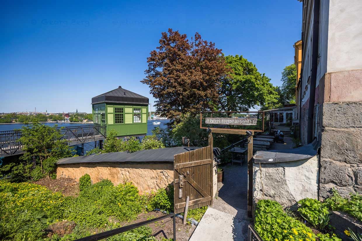 Seiteneingang zur Terrasse des Restaurants Hermans, ein vegetarisches und veganes Restaurant in Stockholm, gelegen in Södermalm an der Fjällgatan 23B. Es bietet mittags ein All-you-can-eat-Buffet mit einer großen Auswahl an pflanzenbasierten Gerichten. Besonders beliebt ist Hermans für seine Terrasse mit Blick auf den Hafen und die Altstadt von Stockholm / © Foto: Georg Berg