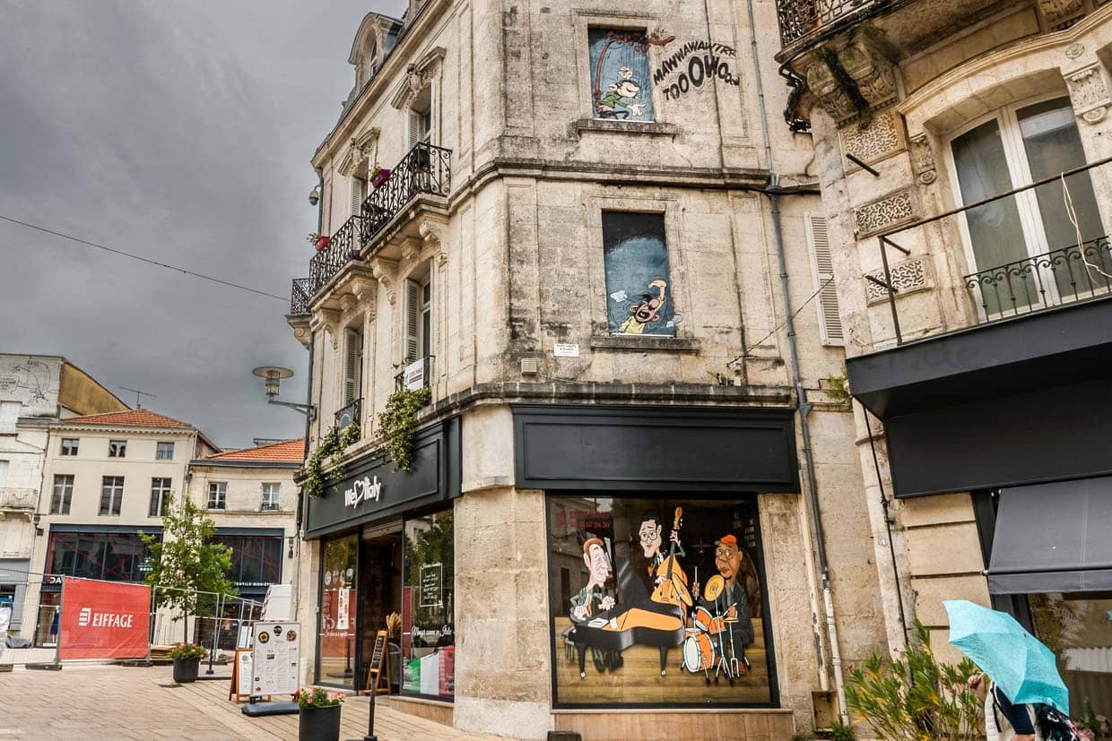 André Franquins Chaos-Duo: Gaston spielt im oberen Fenster auf dem Gaffophon, während Büroleiter Prunelle rot vor Zorn aus dem darunter liegenden Fenster brüllt. Im Hintergrund der abgesperrte Place Marengo, wo Hergé mit einer Statue geehrt wird / © Foto: Georg Berg