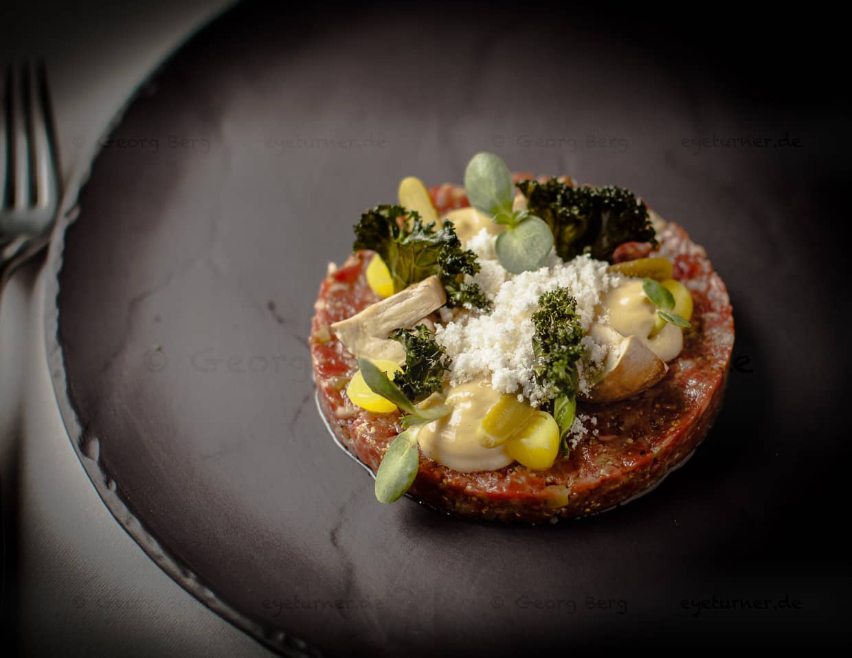 Rindfleisch-Tatar vom lokalen Züchter mit gepickelten Champignons und Gurken. Das Tatar ist gewürzt mit Schalotten, Gurke und französischem Senf und Worchester Sauce. Das Topping besteht aus pulverisierter Nußbutter und frittiertem Federkohl / © Foto: Georg Berg