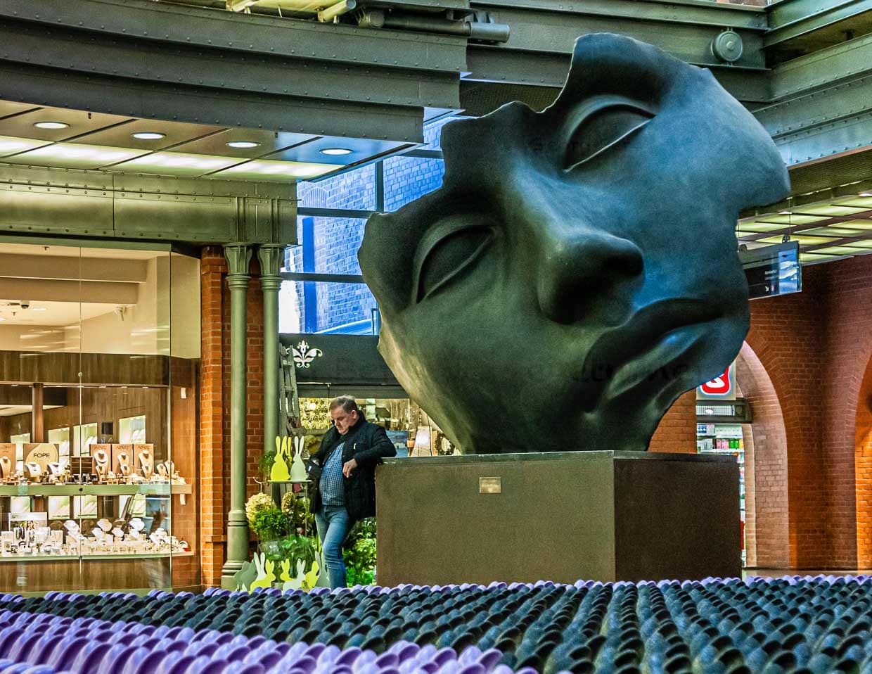 Eine monumentale Maske des polnischen Bildhauers Igor Mitoraj steht mitten in der Shopping Mall der Stary Browar – ein weiteres Beispiel für die Verbindung von Kunst und Gewerbe / © Foto: Georg Berg