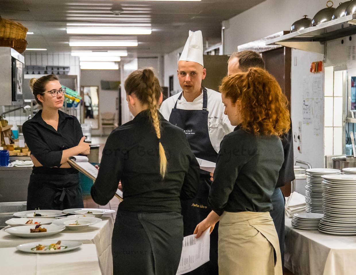 Stefan Lünse, der Küchenchef des Lenkerhofs erläutert den Servicemitarbeitern jeden Abend vor dem Abendessen, welche Gerichte im Gourmetrestaurant Spettacolo zur Auswahl stehen / © Foto: Georg Berg