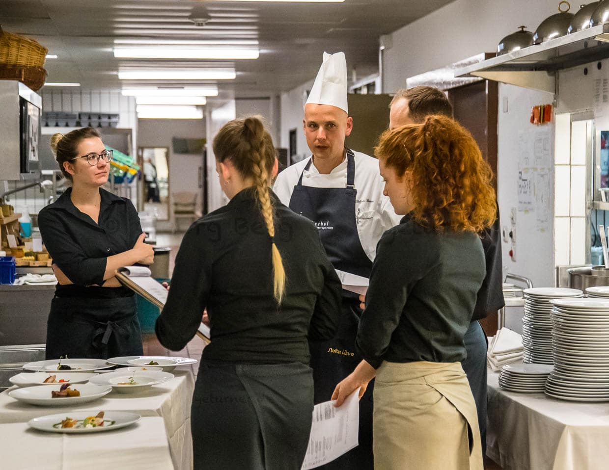 Stefan Lünse, der Küchenchef des Lenkerhofs erläutert den Servicemitarbeitern jeden Abend vor dem Abendessen, welche Gerichte im Gourmetrestaurant Spettacolo zur Auswahl stehen / © Foto: Georg Berg
