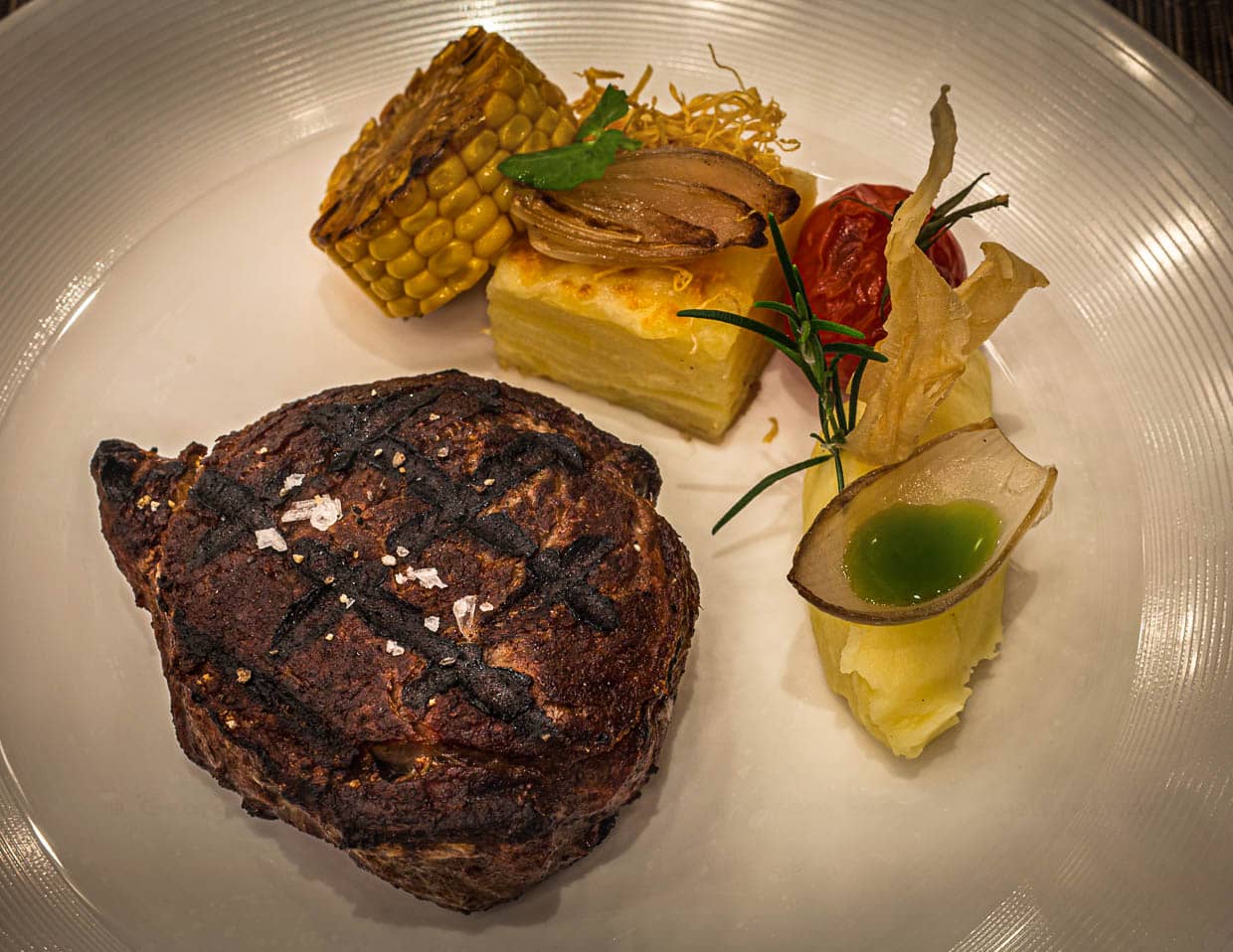 Ribeye vom Black Angus von hauseigener Weide, 28 Tage dry aged mit Kartoffelgratin und Püree mit Basilikumöl im Zwiebel-Schiffchen. Das Fleisch wird am Josper Grill zubereitet / © Foto: Georg Berg