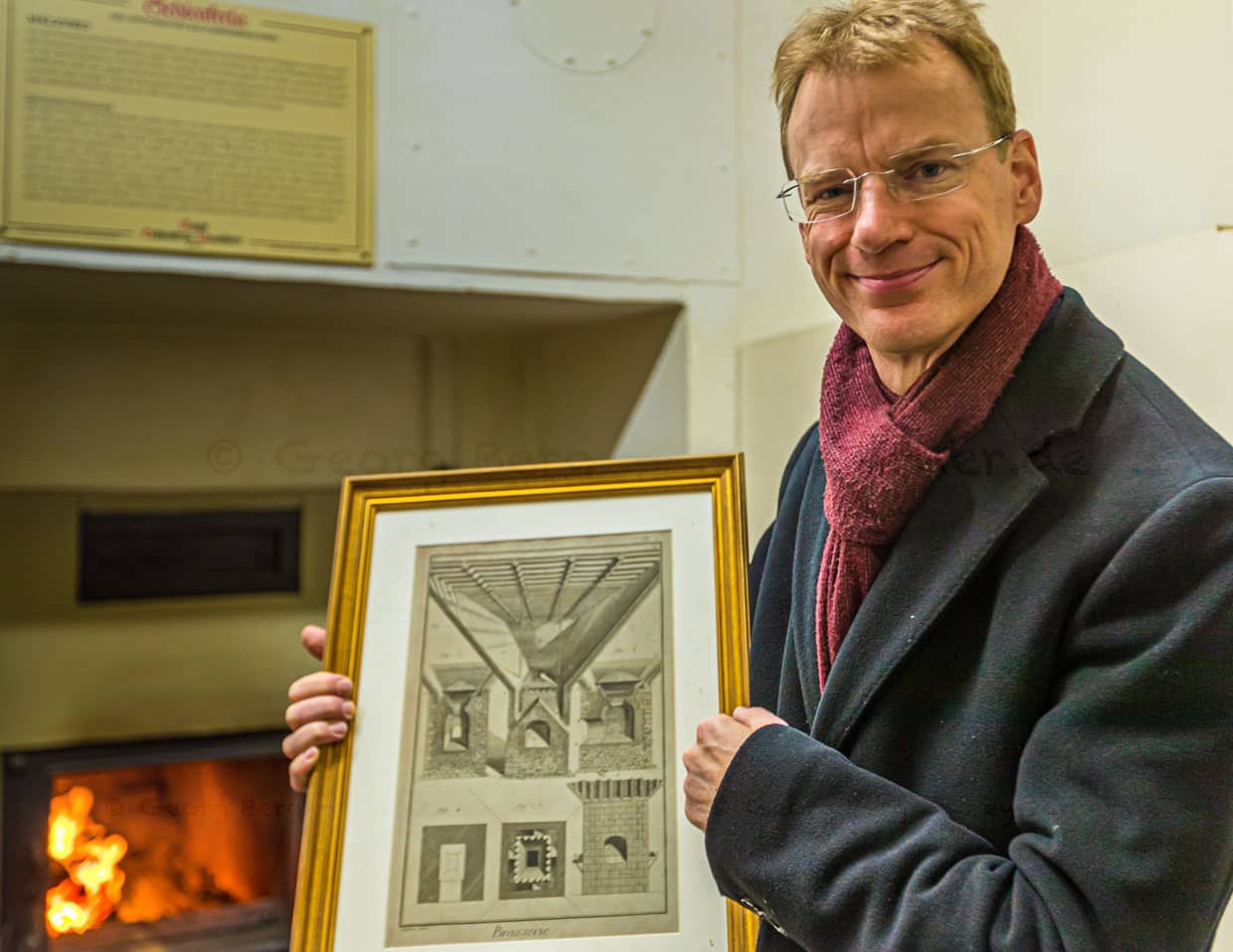Matthias Trum von der Schlenkerla Bräu vor dem Holzofen mit dem das Grünmalz betrocknet wird. In der Hand hält er eine Zeichnung zur industriellen Malztrocknung nach Sir Nicholas Halse / © Foto: Georg Berg