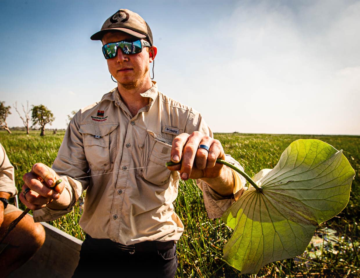 Sam greift ein Lotusblatt, bricht den Stengel durch und zieht aus dem Pflanzensaft einen Faden lang / © Foto: Georg Berg