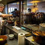 Chef Eric Rousselot bereitet das berühmte Cassoulet Imperial in der Hostellerie Etienne zu, die seit 1956 als Familienbetrieb geführt wird. Dicht an dicht sitzen die Gäste im Restaurant Etienne auch an einem Wochentag im November. Eric Rousselot gießt noch etwas Boullion an, bevor die nächste Cassole an den Tisch geht / © Foto: Georg Berg