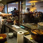 Chef Eric Rousselot bereitet das berühmte Cassoulet Imperial in der Hostellerie Etienne zu, die seit 1956 als Familienbetrieb geführt wird. Dicht an dicht sitzen die Gäste im Restaurant Etienne auch an einem Wochentag im November. Eric Rousselot gießt noch etwas Boullion an, bevor die nächste Cassole an den Tisch geht / © Foto: Georg Berg