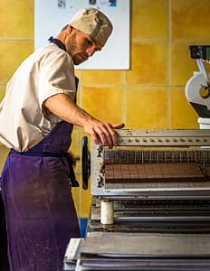 Mitarbeiter der Chocolaterie Frigoulettte in Beaufort-sur-Gervanne beim Zuschnitt von Nougat-Pralinen. Die geschnittene Praline kommt ohne eine zusätzliche Schokoladenhülle aus. Die Manufaktur verwendet ausschließlich biozertifizierte und fairtraide gehandelte Kakaobohnen aus São Tomé / © Foto: Georg Berg