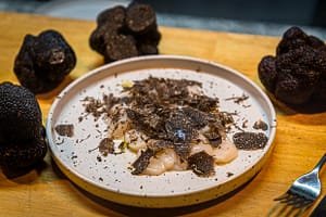 Frische Jakobsmuscheln gewürzt mit Meersalz, schwarzem Pfeffer und Olivenöl sowie frisch gehobeltem schwarzen Trüffel.  Reduziert auf diese wenigen Zutaten kommt das Aroma des schwarzen Trüffels sehr gut zur Geltung / © Foto: Georg Berg