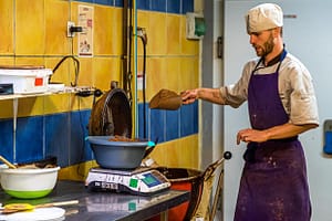 Ein Mitarbeiter der Chocolaterie Frigoulette wiegt Zutaten für die berühmte Malakoff-Praline ab. Bei Frigoulette werden keine tierischen Fette wie Milch, Sahne oder Butter verarbeitet. Auch Palmöl kommt nicht zum Einsatz. Stattdessen 68 prozentiger Kakaoanteil und echte Kakaobutter aus São Tomé / © Foto: Georg Berg