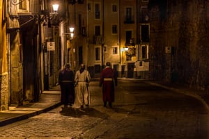 Drei Personen in Prozessionstrachten gehen nachts durch eine spanische Gasse. / © Foto: Georg Berg
