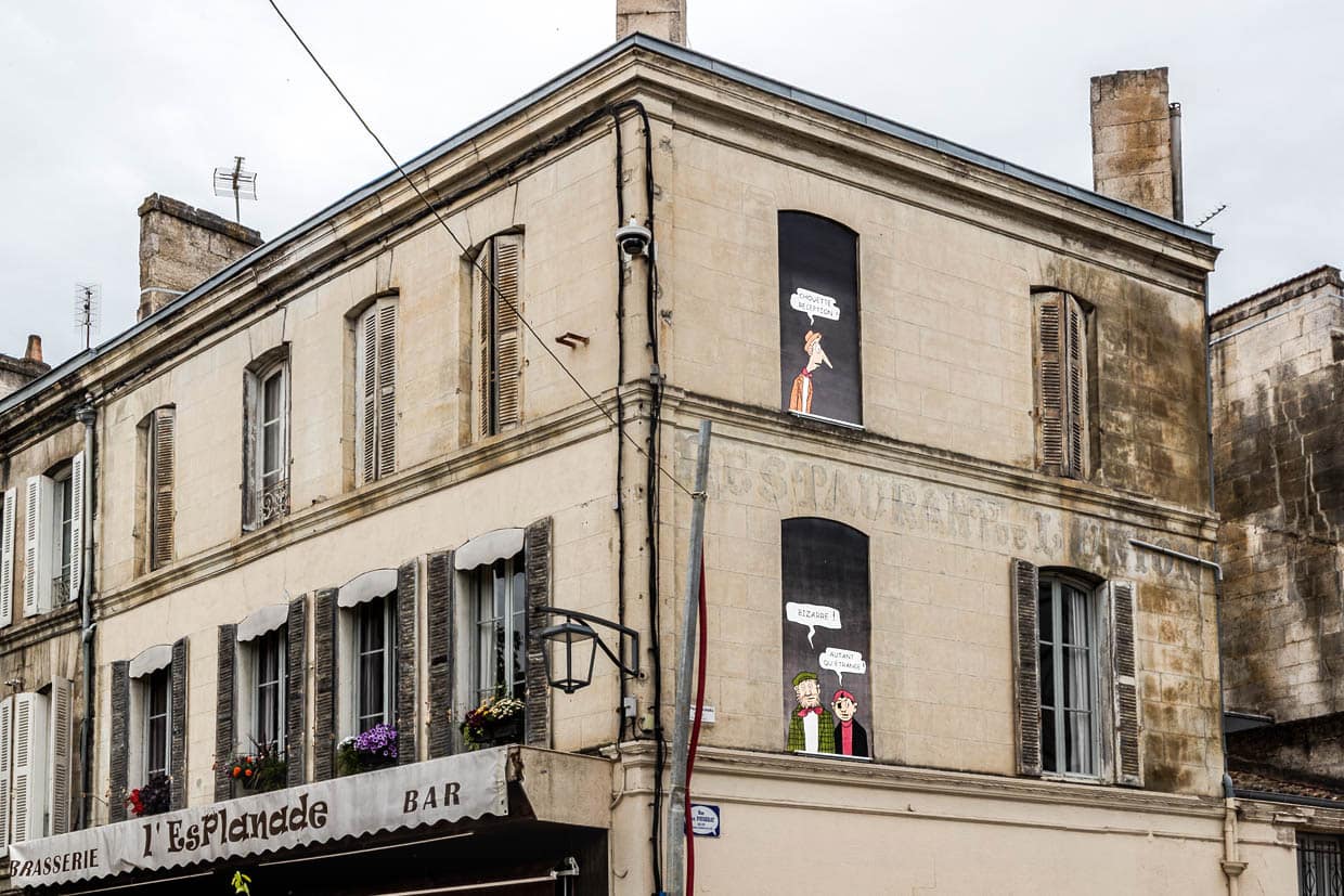 Trompe-l'œil-Perfektion in der Rue Louis Barthou: Die „Pieds Nickelés" – Ribouldingue, Filochard und Croquignol – führen in gemalten Fenstern über der Brasserie L'Esplanade ihre Gespräche. „Tolle Begrüßung!" – „Seltsam!" – „So seltsam wie nur möglich." / © Foto: Georg Berg