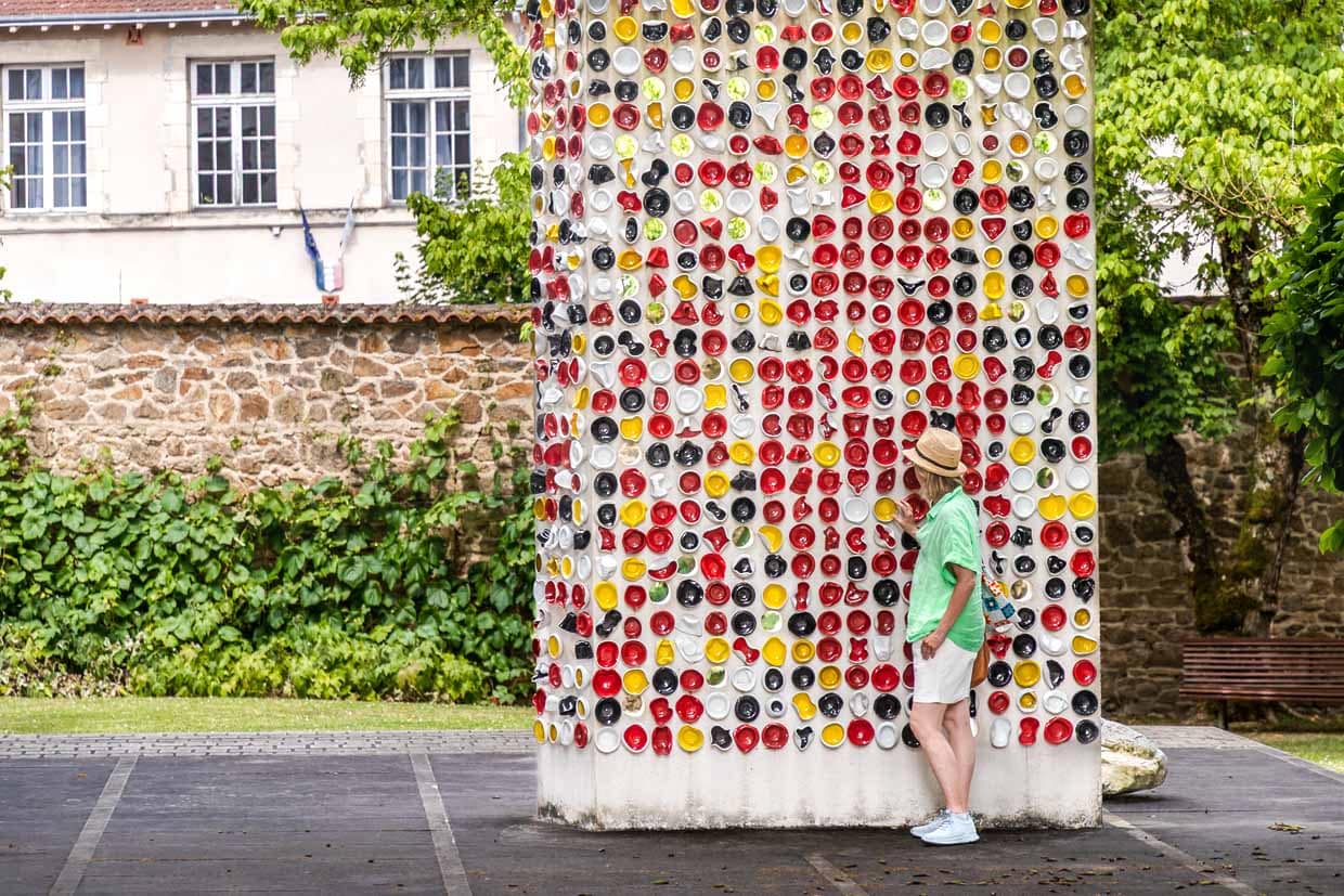 Kunstinstallation „Une Suite“ von den Künstlern Haguiko und Jean-Pierre Viot. Sie besteht aus farbigen, teils deformierten Porzellanschälchen, die an einer hohen, weißen Betonstele aufgehängt sind. Insgesamt umfasst das Werk etwa 600 Porzellanschalen in verschiedenen Farben und Formen, Musée National Adrien Dubouché in Limoges / © Foto: Georg Berg